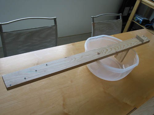 A homemade banjo consisting of a wooden plank, plastic tub, fishing line, screws and a metal bridge