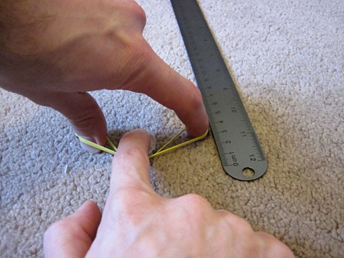 A rubber band stretched between two fingers on a carpet next to a ruler