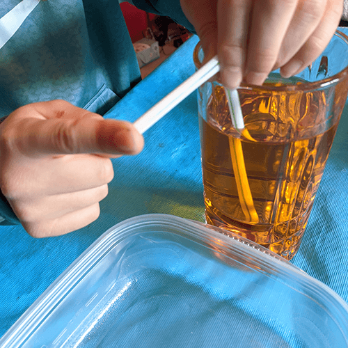 Student holding finger over the end of a siphon made out of straws and placed in a tall cup filled with colored water