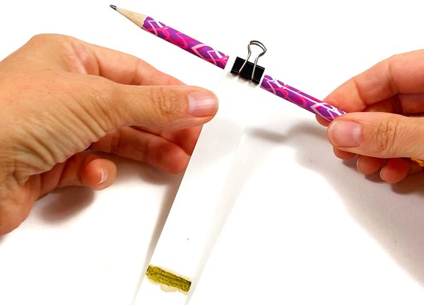 A paper strip is attached to a pencil with a binder clip.