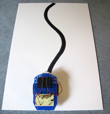 A line-following robot is placed on a white paper with a large black line drawn with multiple curves