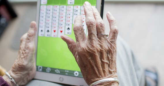 Elderly person's hands playing a memory game on a device