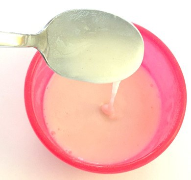  A spoon with a runny paste flowing into a small bowl. 