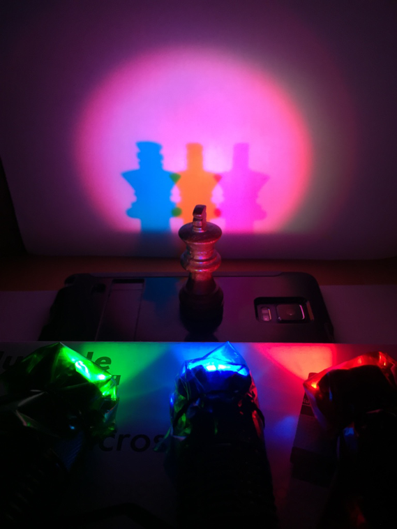 Three light sources casting colored shadows of an object on the wall