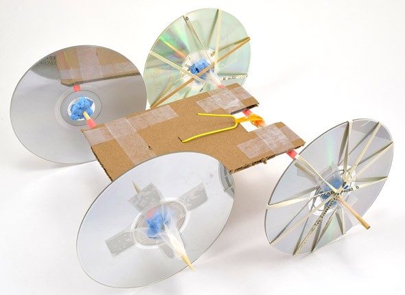 A homemade rubber band powered car made from CDs, cardboard, paperclips, tape, wooden skewers and rubber bands