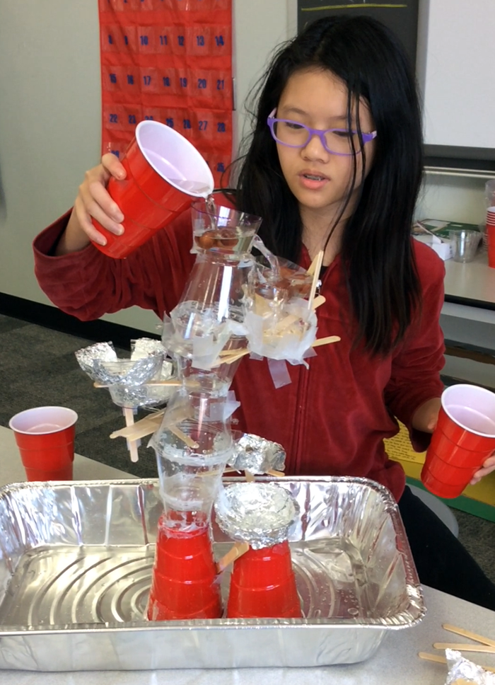 A student pours water into the top of a tower made from plastic cups, tape and aluminum foil