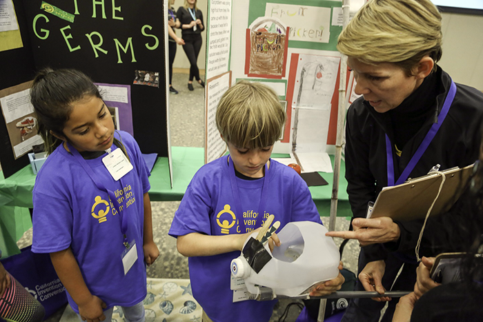 A woman talking to two students in front of a display board