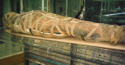 A partially wrapped and mummified Egyptian body resting on a platform