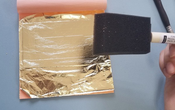 Laying metal leaf on vinyl tattoo sheet and dabbing with dry foam brush 