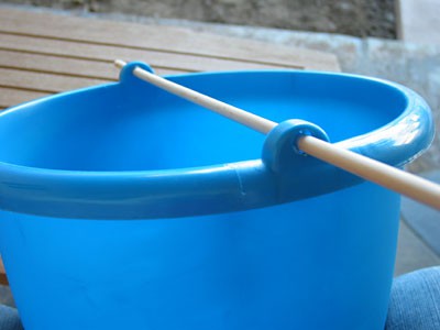 A wooden dowel inserted through two holes near the rim of a plastic bucket
