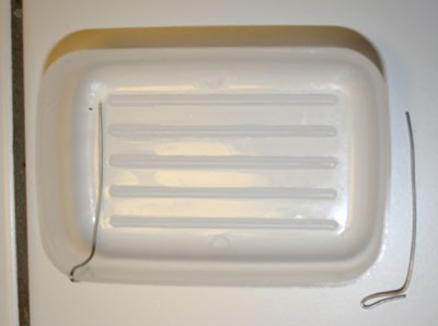 Two stainless steel wires are bent so one side can hook onto the wall of a shallow container and the other side lays flat