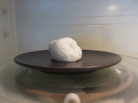 A marshmallow puffed up after cooking in the microwave on a plate