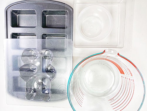 A baking pan for mini loaves, a plastic square tile mold, a plastic food container, and a glass liquid measuring cup.