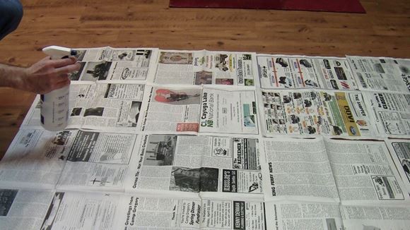 Spray bottle being held above the newspaper on the floor.