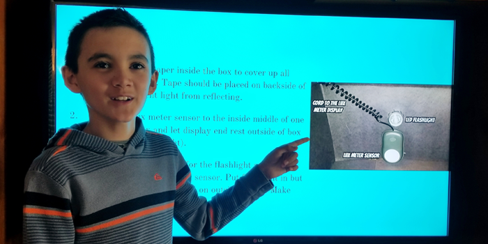 A students points to an image on a PowerPoint presentation projected behind him