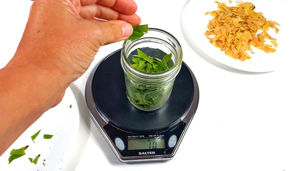 A mason jar filled with cut green leaves is sitting on a scale. The scale shows 10 grams.