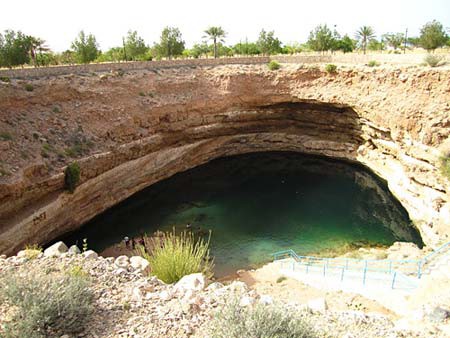 Domed rock forms a roof over a body of water at the bottom of a sinkhole
