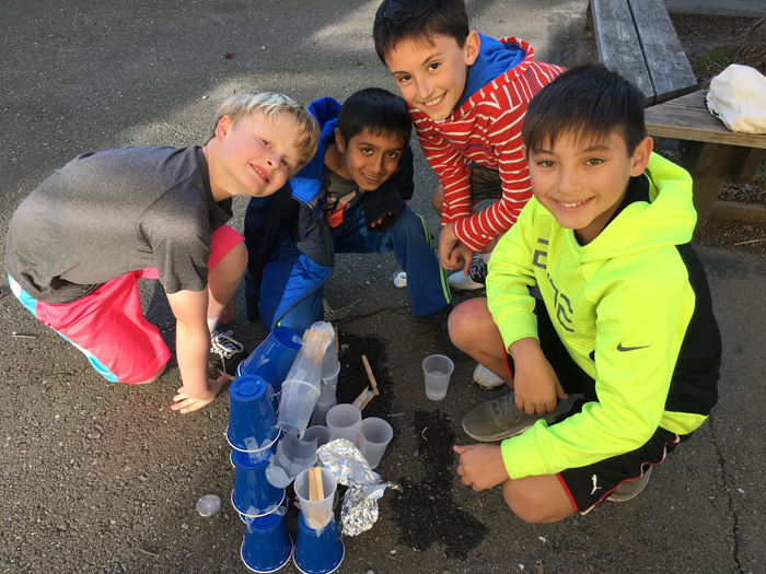 Four students next to four towers made from plastic cups, tape and aluminum foil