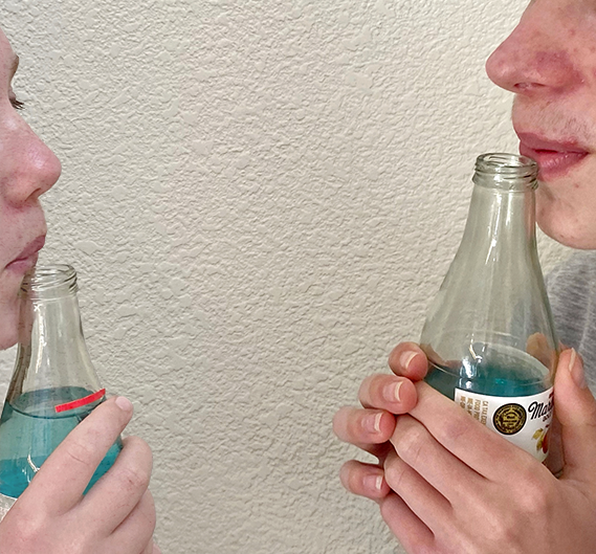 Two kids blowing across the top of bottles filled with different amounts of colored liquid