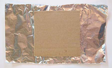 A cardboard square is placed in the center of a sheet of aluminum foil