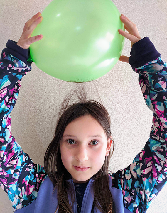 physics experiments electricity Girl rubbing a balloon on her head and hair standing up from static electricity.