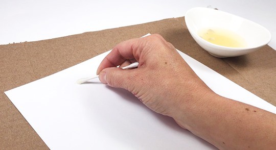 A hand holding a Q-tip and writing a message onto a white sheet of paper.