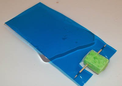 A toothpick is inserted through a small piece of sponge and taped to a blue plastic sheet