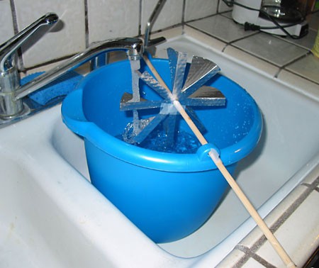 Water from a sink flows over a homemade water wheel in a bucket