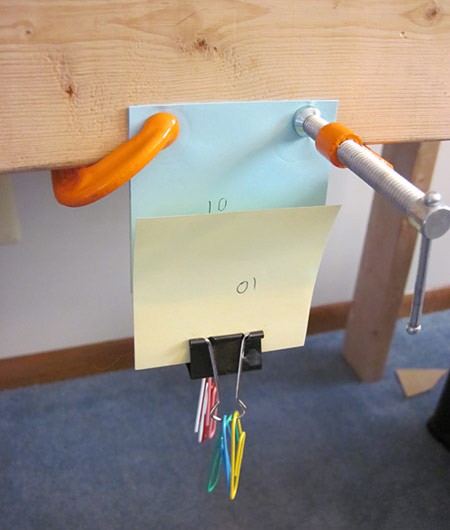 One end of a interlaced paper pad is clamped to a wood frame while paperclips are placed on the bottom end