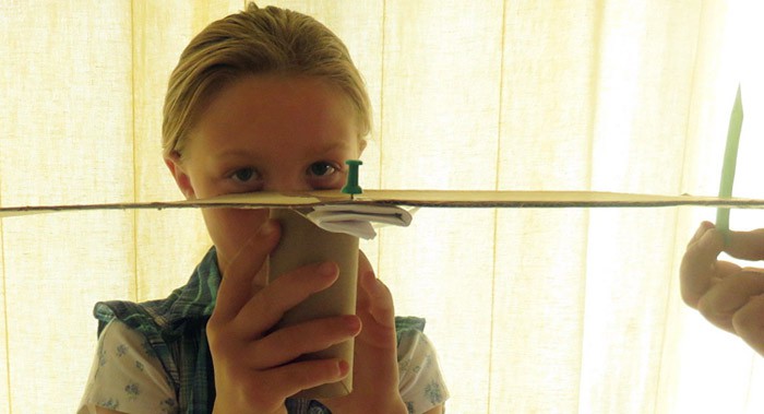 A child stares at a push pin across a large protractor while a colored paper is moved along the edge of the protractor