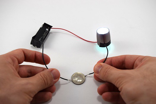 A battery, small light, and nickle connected with three wires.