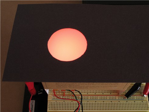 Red light shines through a circle cut into black paper that has been placed over a translucent white block