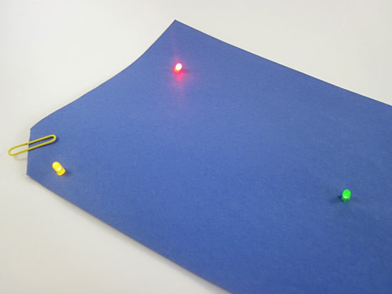 Three LEDs and a paper clip sit on the surface of a sheet of paper