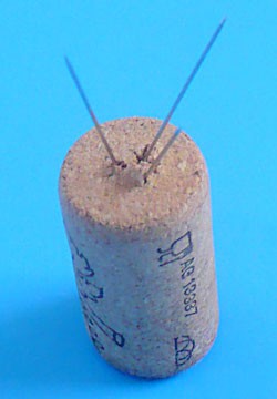 Three metal needles are stuck into one end of a piece of cork