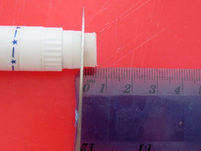 A small section of lip balm is cut from a tube using a knife