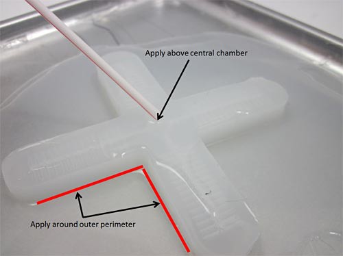 Photo of uncured silicon added around the edges and in the center of a cross-shaped silicon mold