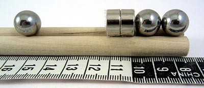 A metal ball bearing next to a group of two metal ball bearings attached to two circular magnets