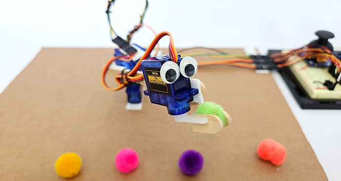 A robotic arm made from servo motors and popsicle sticks picking up a pom-pom 