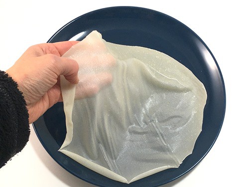 A hand placing a sheet of slightly translucent edible paper on a plate.