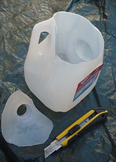 A utility knife is used to cut the top off of a plastic water jug
