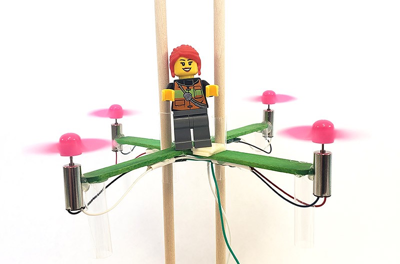 A LEGO mini figure riding on a popsicle stick drone.