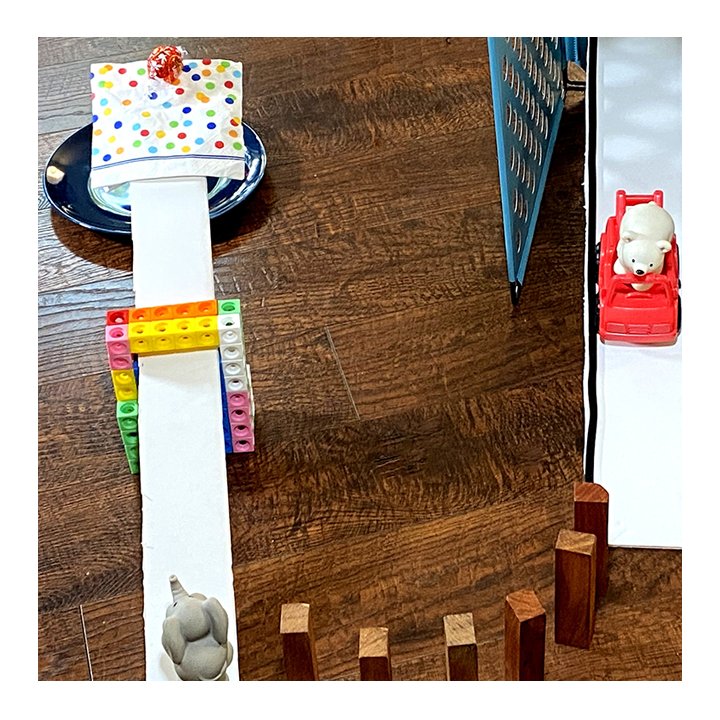 Sample Rube Goldberg machine where a small toy rolls down a ramp, knocks over dominoes, and triggers another chain reaction - Awesome Summer Science Experiments