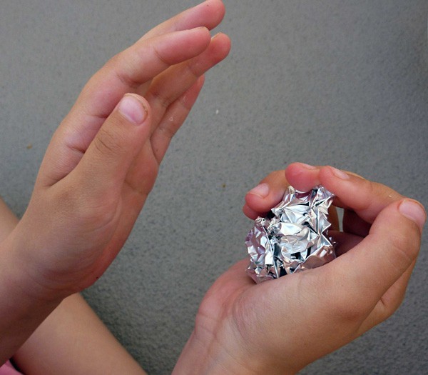 Two hands squeeze aluminum foil into a ball