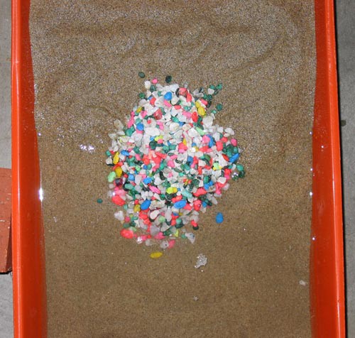 Pile of aquarium gravel on sand within a paint roller pan