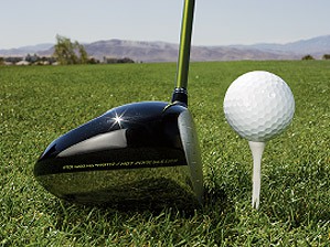 The head of a driver rests slightly below a golf ball on a tee