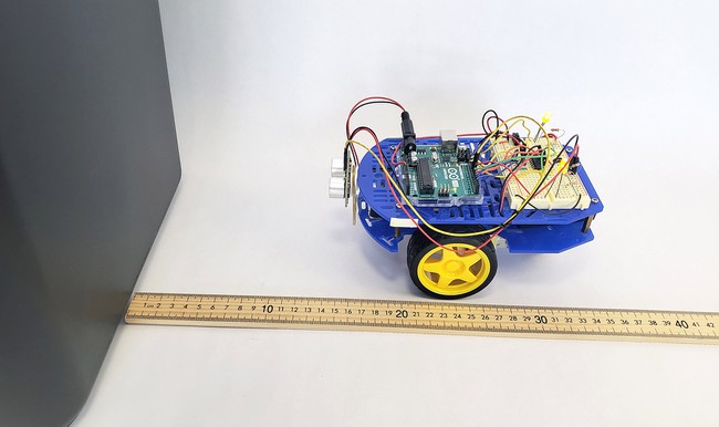 An Arduino robot stopped in front of a trash can with a meterstick measuring the distance 