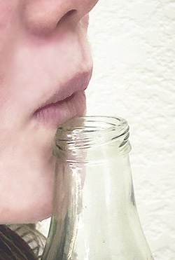 A person blowing across the mouth of a bottle