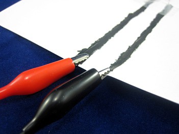 Alligator clips attached to two lines of conductive ink on a piece of paper