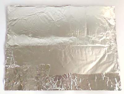 A rectangular piece of cardboard is wrapped in aluminum foil
