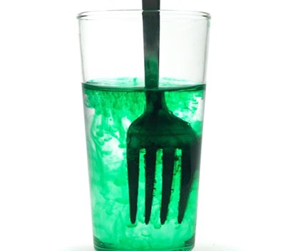 The contents of a glass filled with water-food-coloring mixture are mixed with a fork.